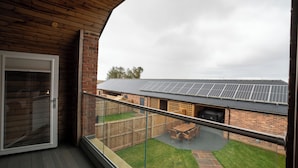 Un balcón con vista a un patio trasero, un edificio de ladrillo y paneles solares en el techo.