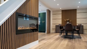 Un interior moderno con una pared de listones de madera, una chimenea, un comedor con mesa y sillas, y una cocina al fondo.