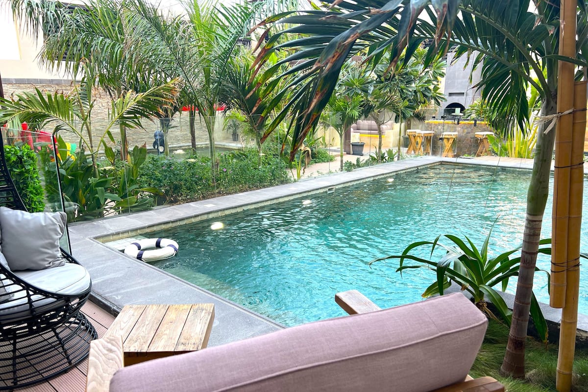 A pool area with a lounge chair, a wooden table, and a cushioned bench.