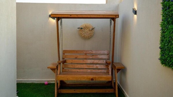 A wooden swing with a canopy, a wall-mounted decorative piece, and a green wall with foliage. - Villa Bali Jeddah (Jeddah)