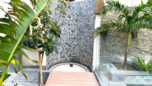Un espacio exterior moderno con pared de piedra, barandilla de cristal y plantas tropicales.
