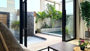 Una sala de estar moderna con un gran ventanal que da a un patio con piscina, pared de piedra y diversas plantas.