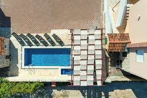 Ein Schwimmbad mit gefliestem Deck, einer Steinmauer und einem roten Ziegeldach.