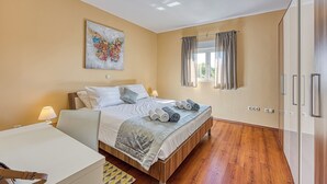 A hotel room with a bed, a desk, a lamp, a window with curtains, and a wall-mounted artwork. - Coastal Paradise Villa With Pool (Sveti Filip i Jakov)