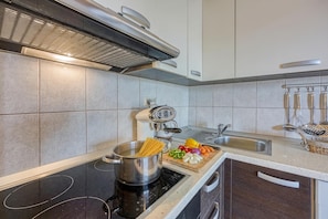 A modern kitchen with a stovetop, a pot of spaghetti, a cutting board with vegetables, and a sink. - Coastal Paradise Villa With Pool (Sveti Filip i Jakov)