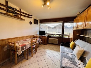 A cozy living room with a dining table, wooden chairs, a sofa, and a television.