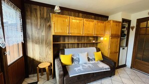 Une pièce confortable avec un lit, des armoires en bois, un petit tabouret et un réfrigérateur.