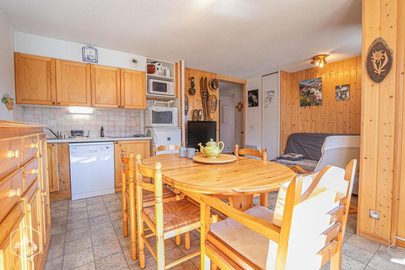 A compact kitchen with wooden cabinets, a microwave, a dishwasher, and a dining area with a wooden table and chairs.