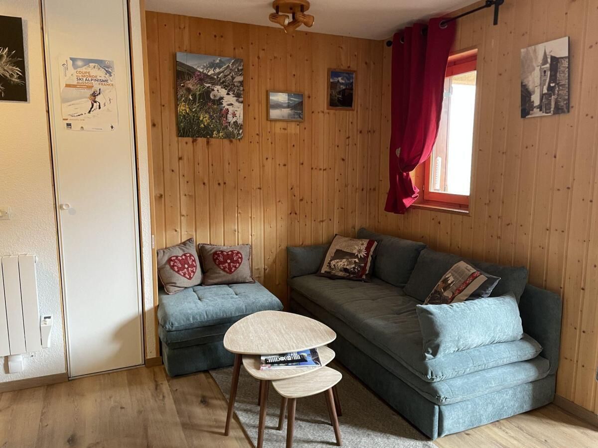 A cozy room with a wooden wall, a grey sofa, a small round table, and a window with red curtains.