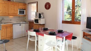 Cozinha compacta com armários de madeira, micro-ondas, cafeteira e mesa de jantar para quatro pessoas.