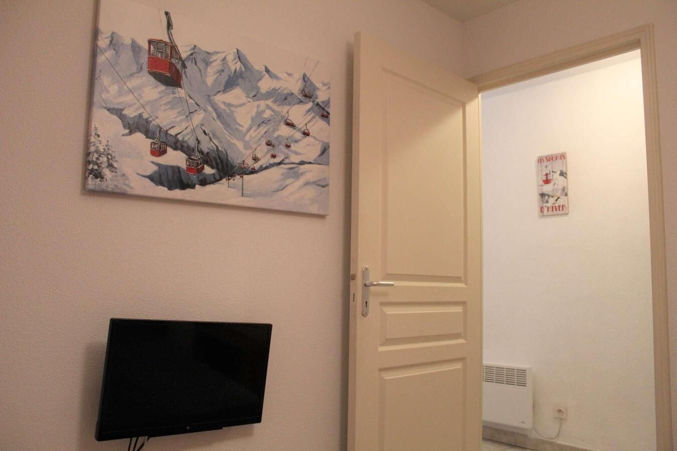 Une pièce avec un téléviseur fixé au mur, une porte et une affiche accrochée au mur.