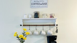 En vit bardisk med en skylt ovanför, en kaffebryggare och burkar på en hylla.