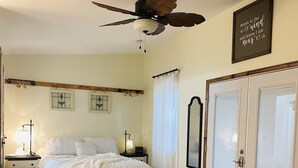 Ett sovrum med en säng, en soffa, en takfläkt, ett nattduksbord, en lampa, en spegel och ett inramat citat på väggen.