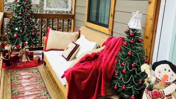 Ett mysigt rum med en träbänk, en säng med ett rött täcke, två julgranar och en snögubbe som dekoration.