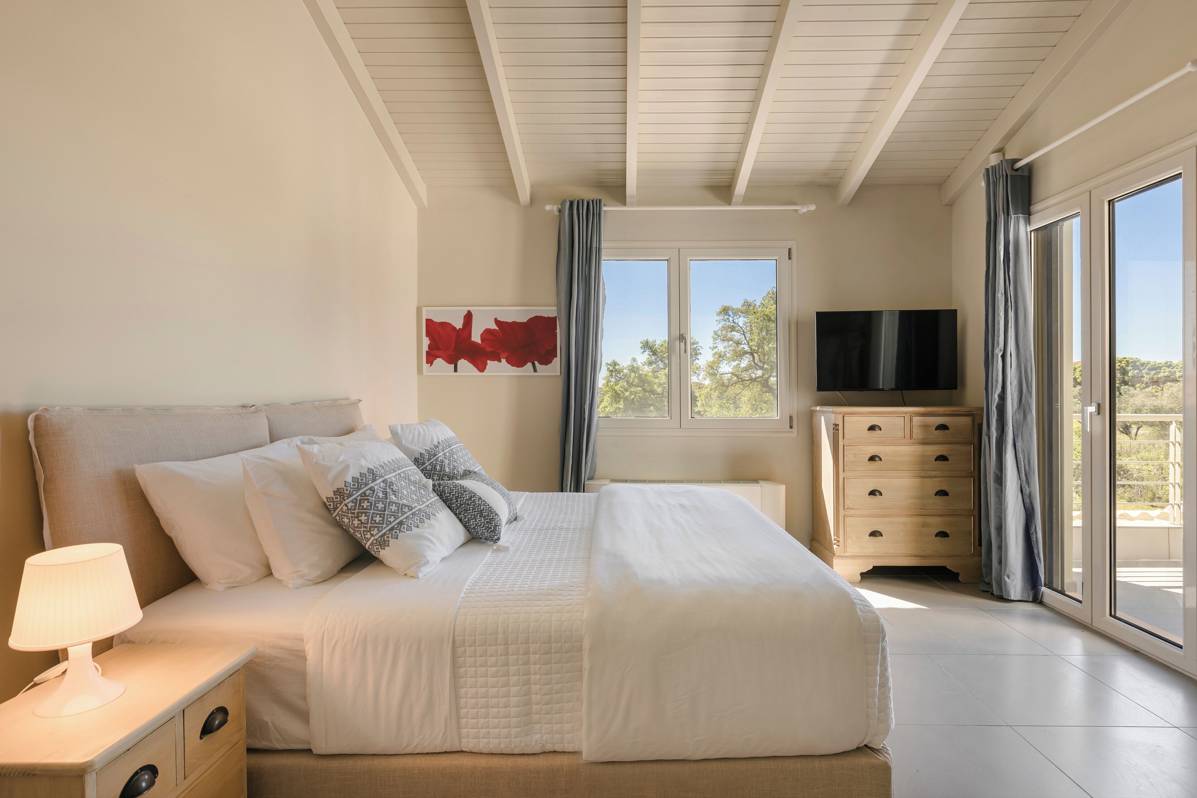 Une chambre à coucher comprenant un lit, une table de chevet, une lampe, une télévision et une commode.