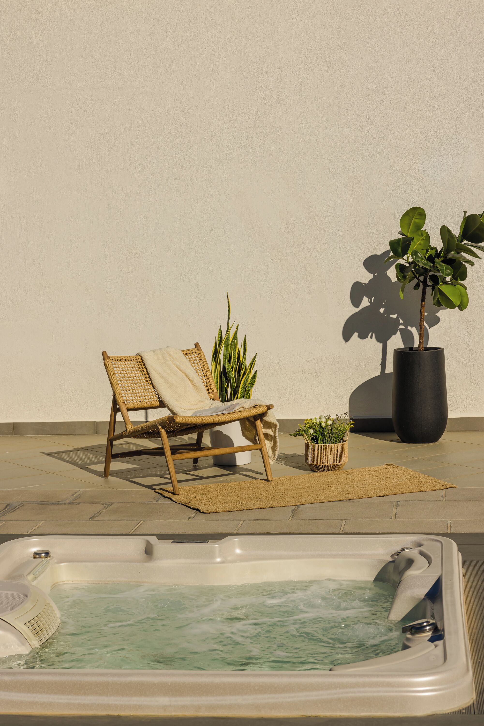A spa area with a hot tub, a wicker lounge chair, and potted plants.