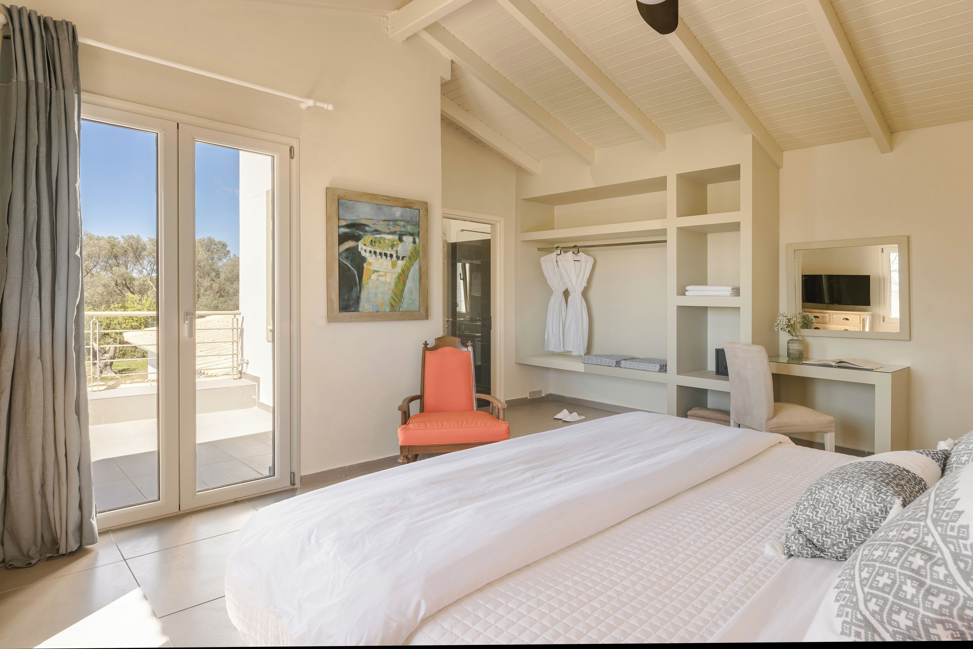 Un dormitorio con una cama grande, una silla, un escritorio y un ventanal corredera que da a un balcón.