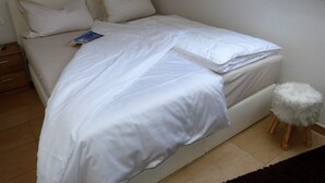 A neatly made bed with white linens and pillows, a small wooden stool, and a window above the bed. - Traumhafte Wohnung Über Zwei Ebenen mit Infrarotkabine, Balkon und Terrasse (Göhren-Lebbin)