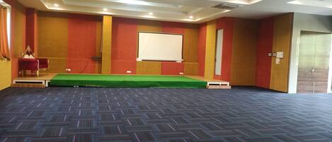 A conference room with a green stage, a white screen, and a red and gold striped wall.