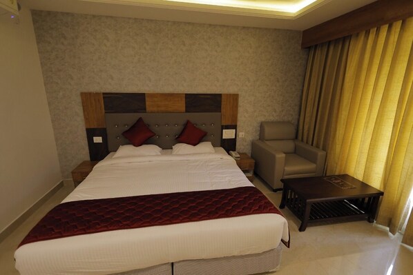 A hotel room with a large bed, a chair, a small table, and a window with curtains.