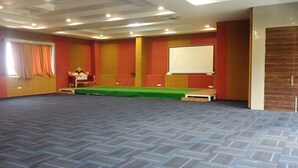 A conference room with a green stage, a whiteboard, and a red and gold color scheme. - Hotel Woodside Prestige Tirupati (Tirupati)