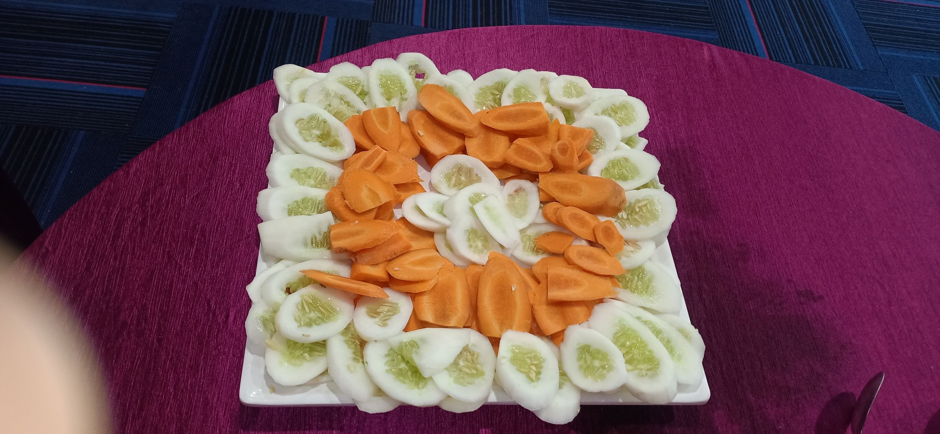 A square plate with sliced vegetables arranged in a heart pattern.