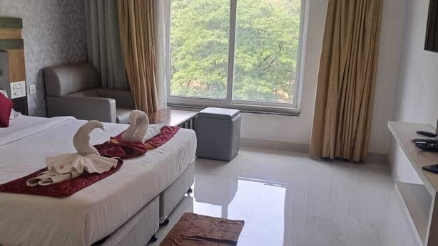 A hotel room with a bed, a sofa, a TV, and a window with curtains. - Hotel Woodside Prestige Tirupati (Tirupati)