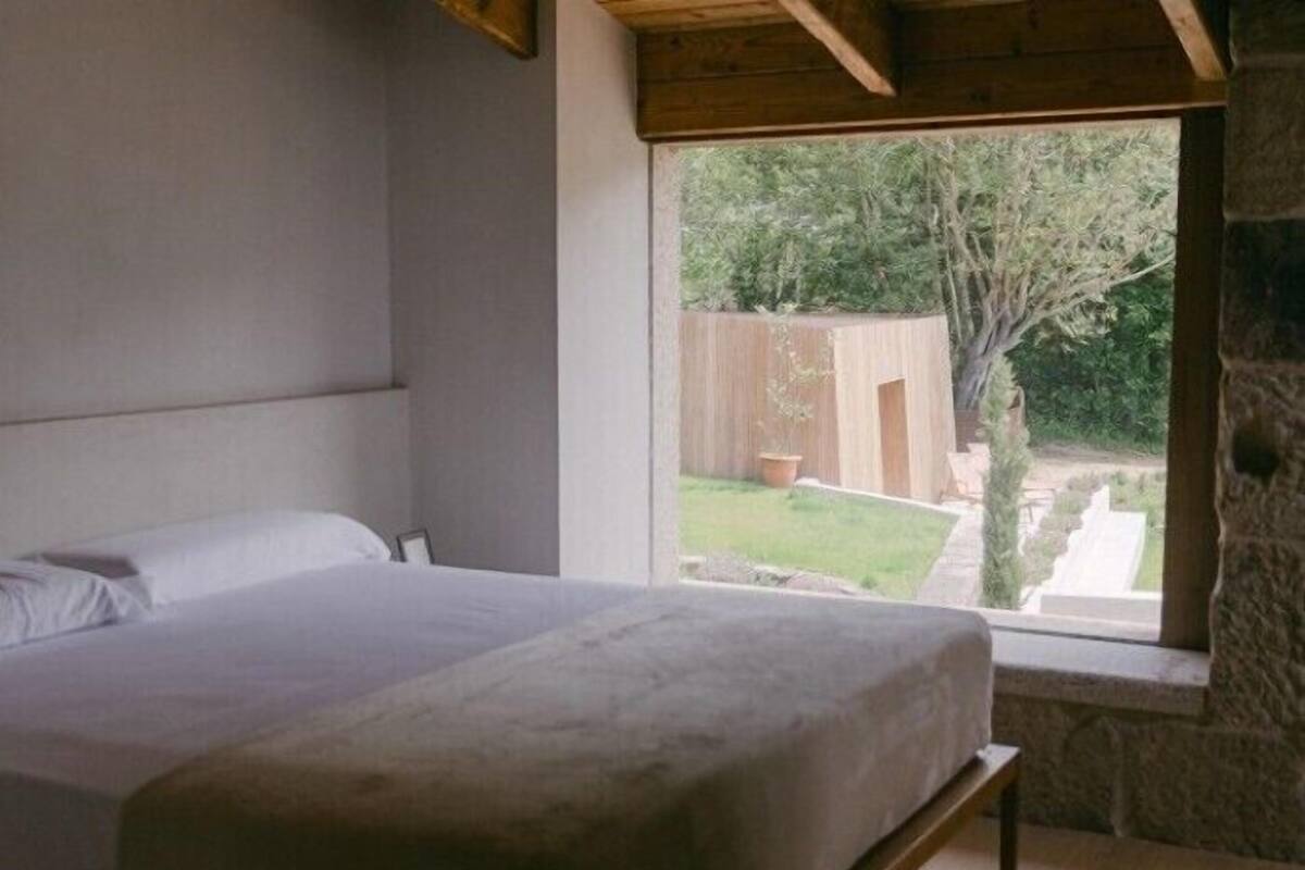 Un dormitorio con cama, ventana y vistas a un jardín.