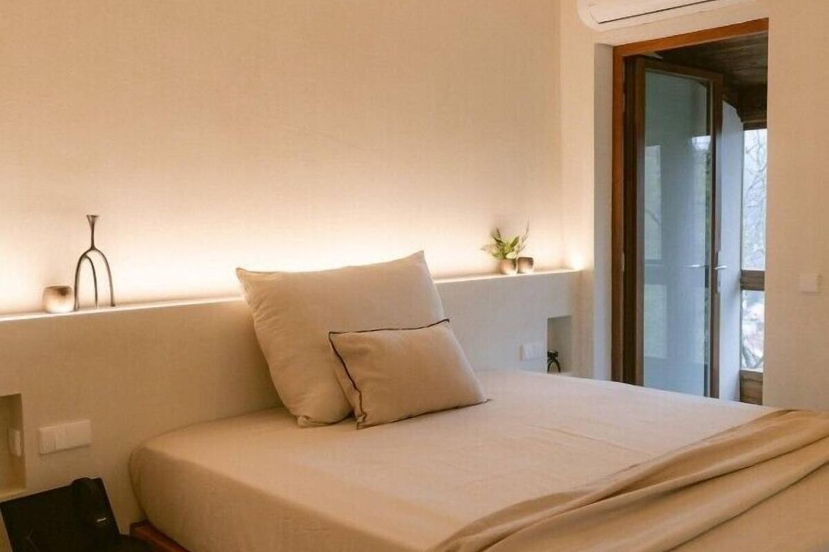 Un dormitorio con cama, mesita de noche, lámpara y ventana con vistas.
