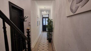 A hallway with patterned floor tiles, a chandelier, a staircase with black balusters, and a large abstract painting on the wall. - Appartement Vilvoorde Centrebrussels Airport (Vilvoorde)