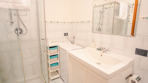Een moderne badkamer met een douchecabine van glas, een wit wastafelmeubel met een spiegel erboven en een wc-rolhouder aan de muur.