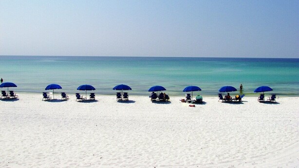 A beach with rows of sun loungers under blue umbrellas. - Paradise Reef Private Pool! Walk to the Beach! Sleeps 10! Jacuzzi! Pet Friendly! (Miramar Beach)