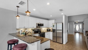 A modern kitchen with white cabinets, stainless steel appliances, granite countertops, and pendant lighting. - Paradise Reef Private Pool! Walk to the Beach! Sleeps 10! Jacuzzi! Pet Friendly! (Miramar Beach)