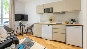 A compact kitchen with a dishwasher, microwave, and a small dining area with a table and chairs. - Sweett | Wagram Cosy (Paris)
