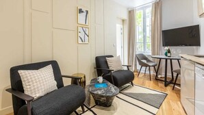 A modern living room with two armchairs, a coffee table, and a TV. - Sweett | Wagram Cosy (Paris)
