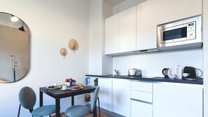 A compact kitchen with a microwave, toaster, and kettle. There is a dining table with chairs and a mirror on the wall. - Sweett | Classy Duomo II (Milano)