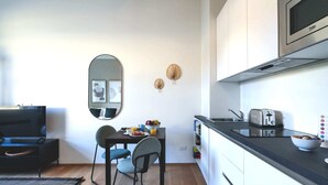 A compact kitchen with a microwave, toaster, and a small dining area with a table and chairs. - Sweett | Classy Duomo II (Milano)