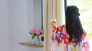 A room with a large window, a mirror, and a vase with pink flowers on a shelf. - Vila Mia (Sarandë)