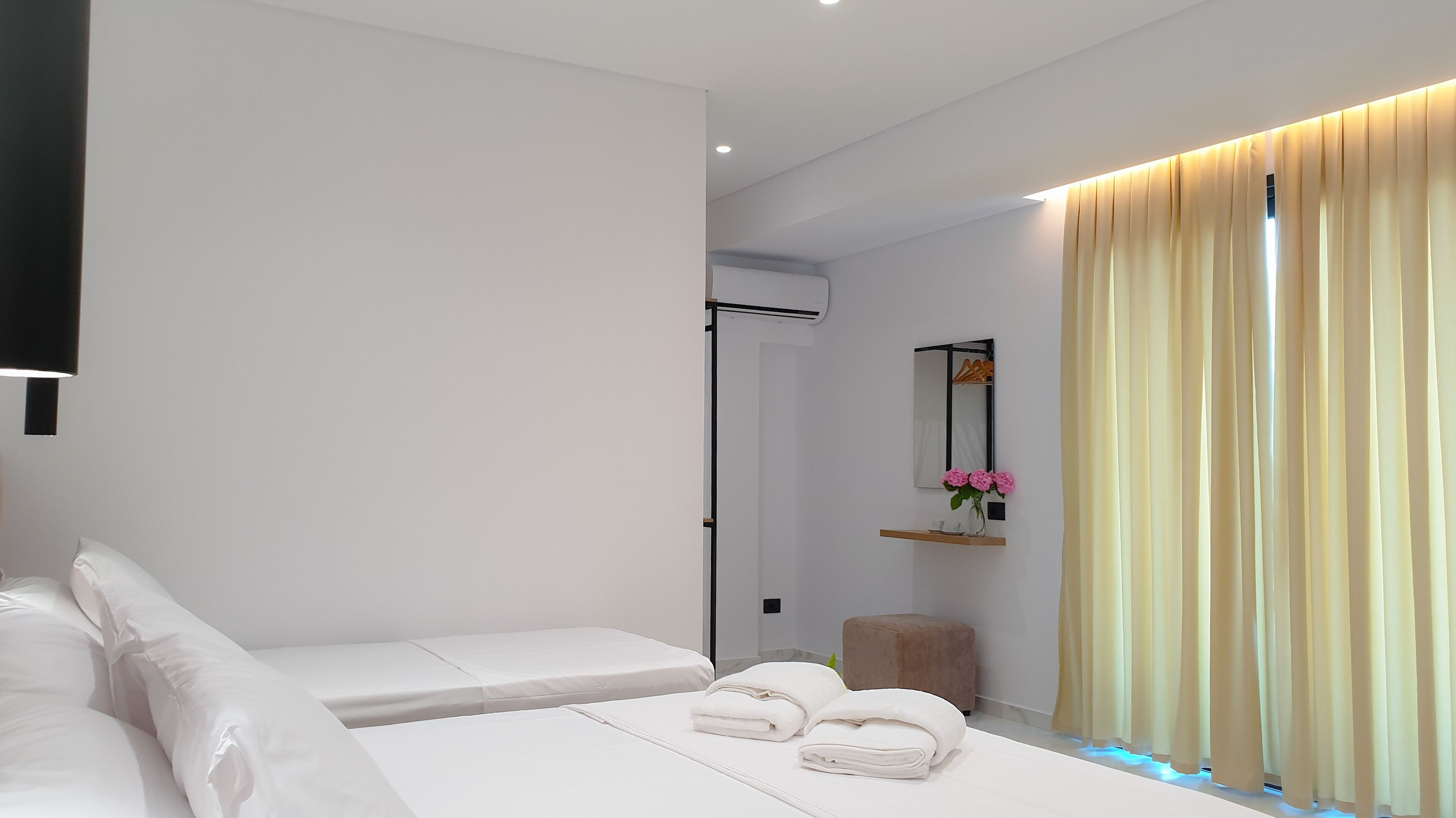A modern bedroom with a bed, a bedside table, a mirror, and a window with curtains.