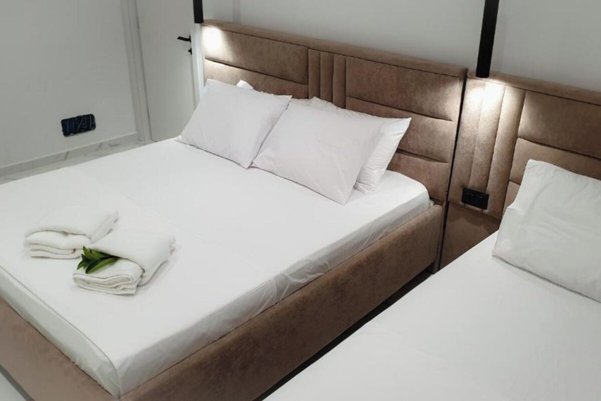 A double bed with white linens and pillows, a wooden headboard, and a bedside table with a lamp.