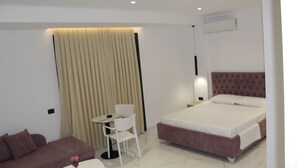 A modern hotel room with a bed, a sofa, a chair, a small table, and a wall-mounted air conditioner. - Vila Mia (Sarandë)