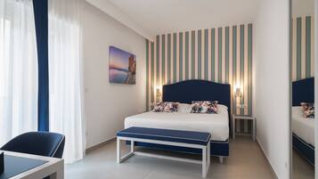 A modern hotel room with a large bed, bedside tables, a bench, a desk, and a large mirror.
