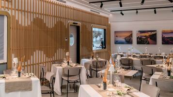 A dining area with multiple tables set for a meal, featuring a modern interior with wooden paneling and artwork on the walls.
