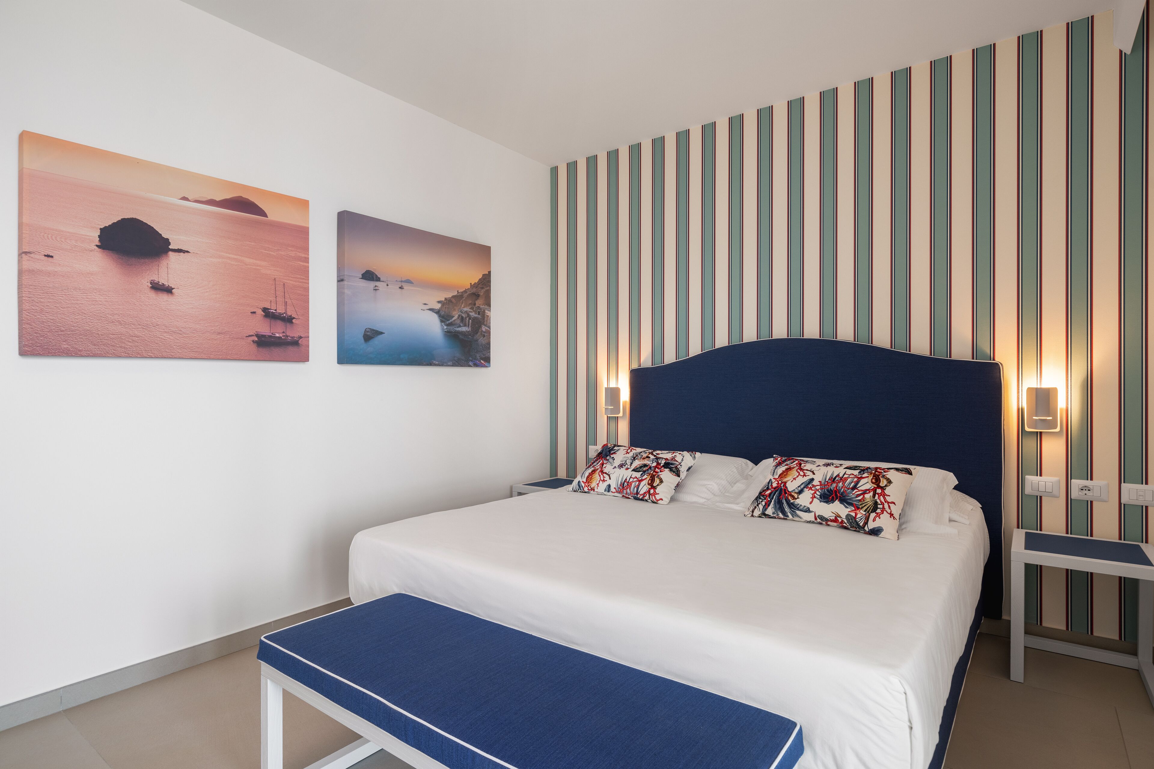 Een slaapkamer met een bed, een bankje en twee aan de muur hangende schilderijen.
