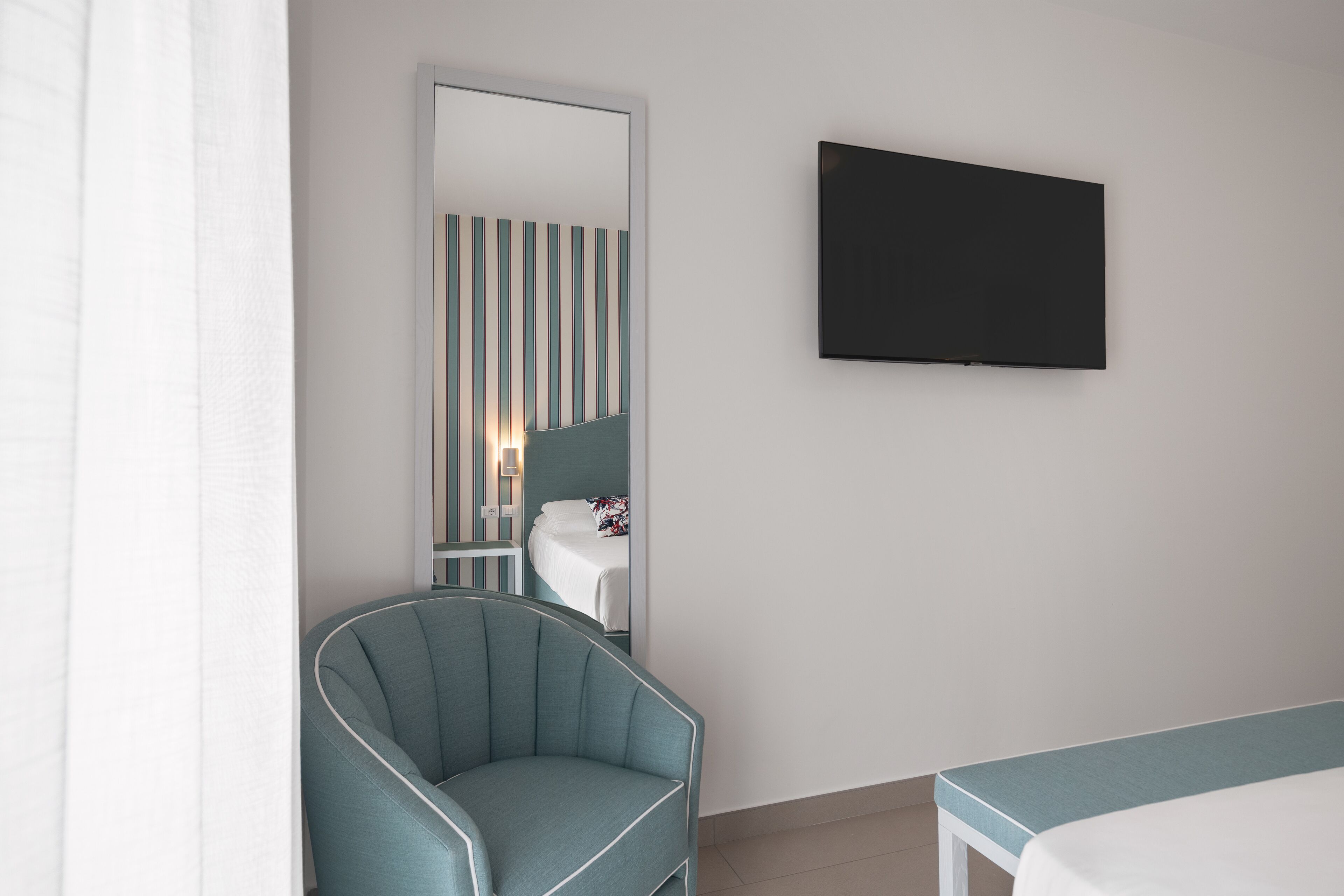 Une chambre d’hôtel avec un lit, une chaise, une télévision et un miroir.