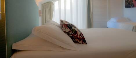 A hotel room with a bed, a headboard, a window with curtains, and a painting on the wall.