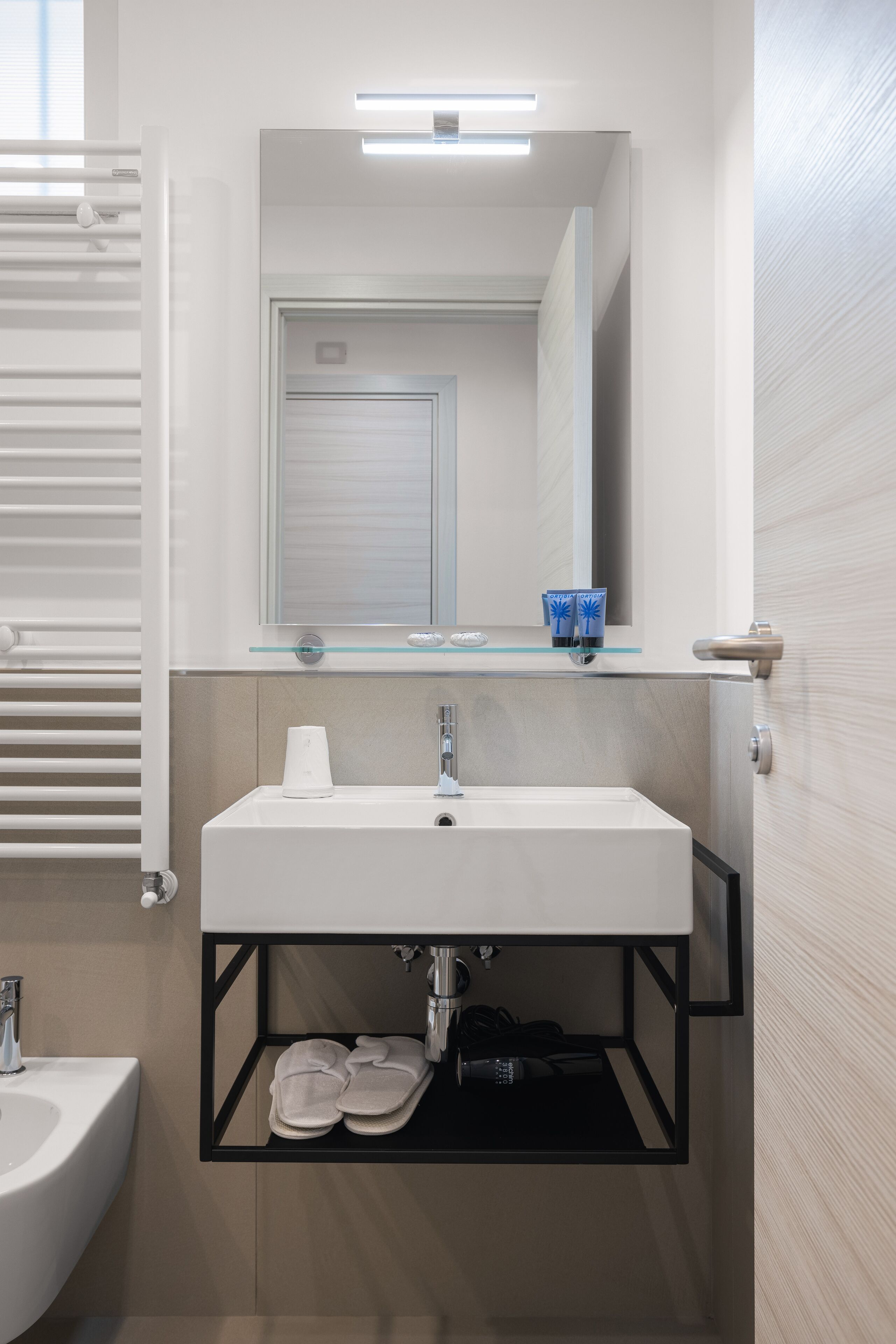 A modern bathroom with a white sink, a glass shelf with toiletries, and a mirror above it.