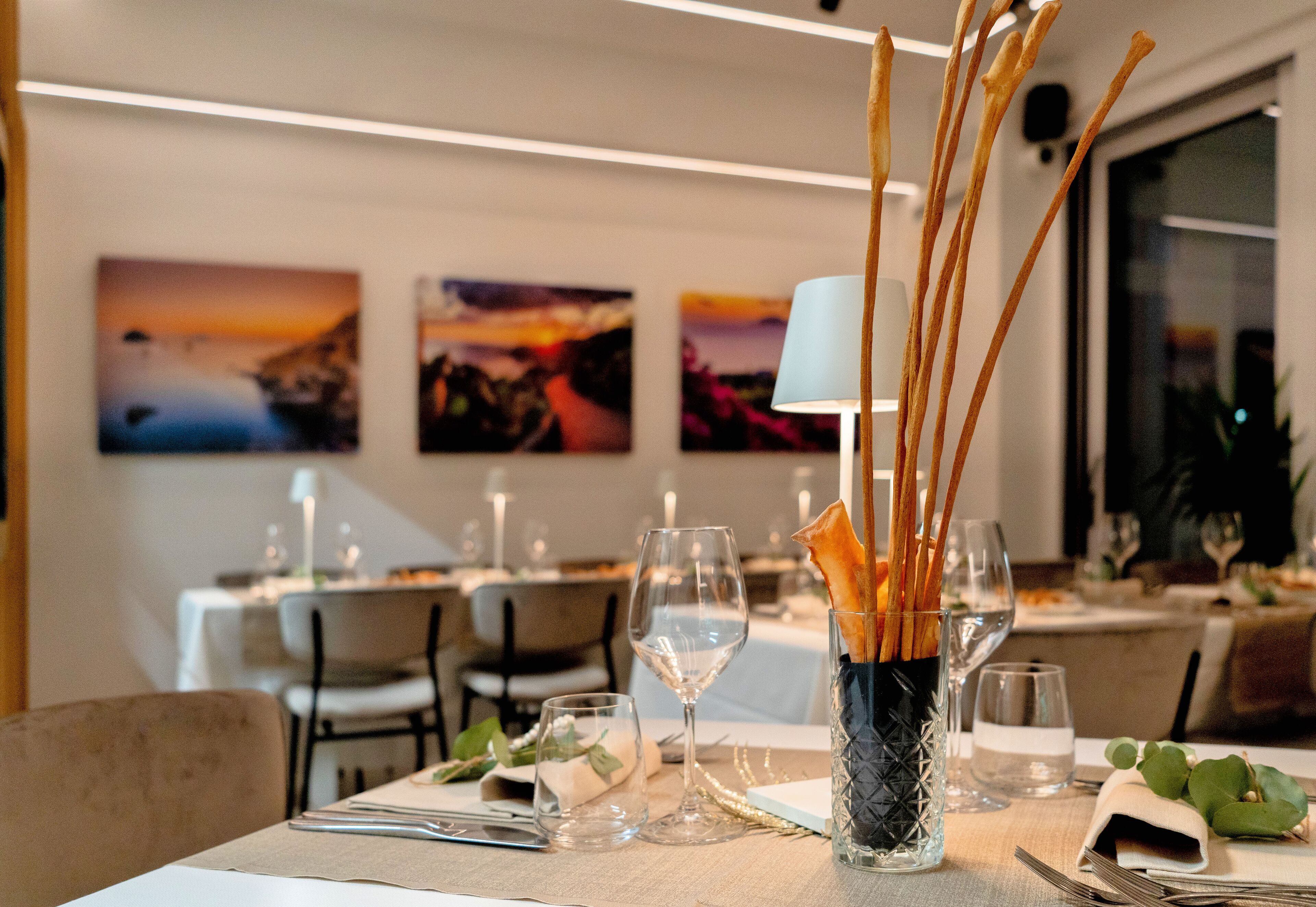 Una mesa de comedor dispuesta con copas de vino, un florero con ramas y una vela.