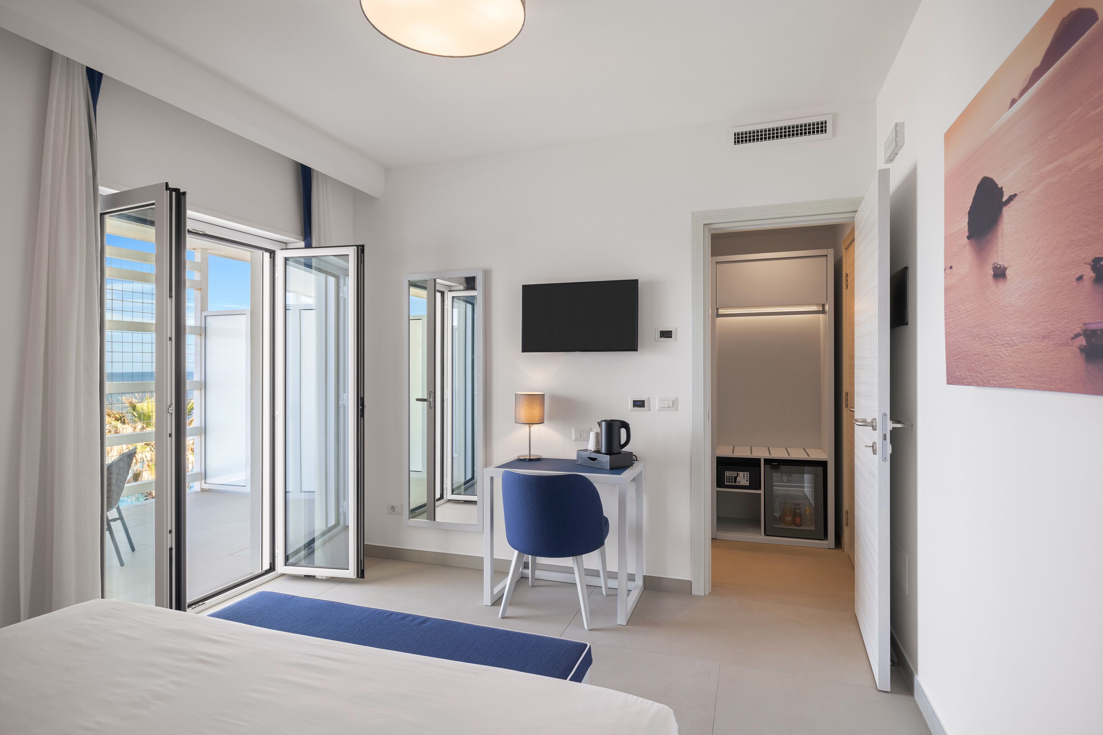 Habitación de hotel moderna con cama, escritorio con lámpara, televisión y puerta corrediza a un balcón.