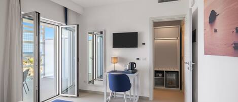 Habitación de hotel moderna con cama, escritorio con lámpara, televisión y puerta corrediza a un balcón.
